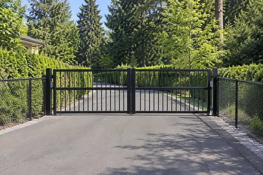 Black double-leaf gate across a paved driveway surrounded by trees