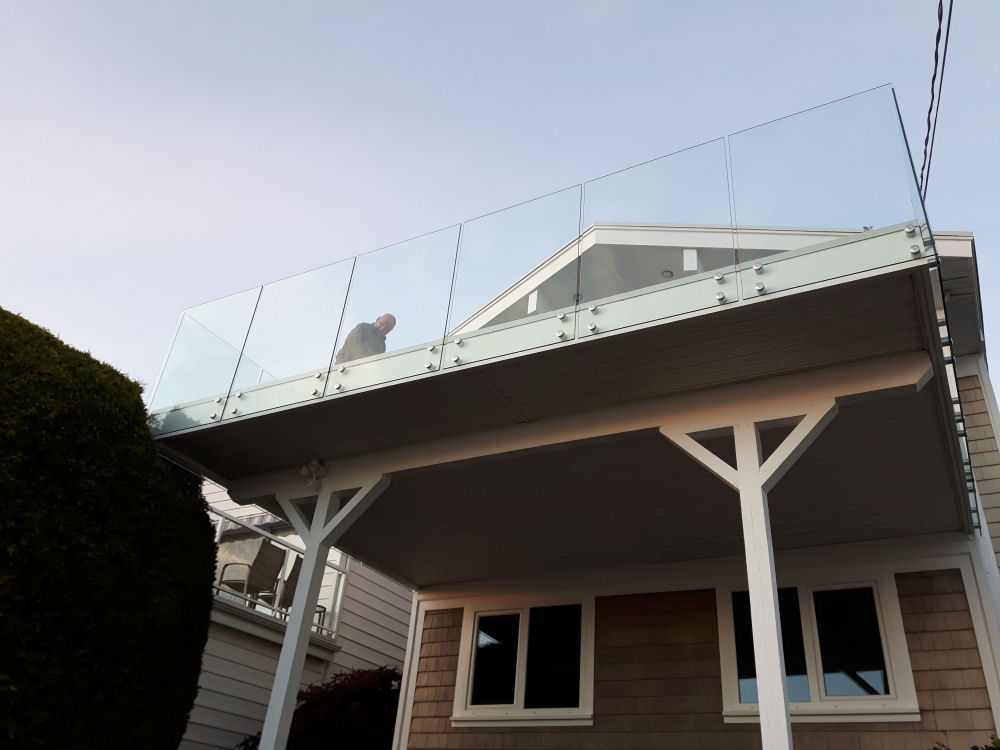 House with a second-floor glass balcony, where a person stands looking outward. The structure is