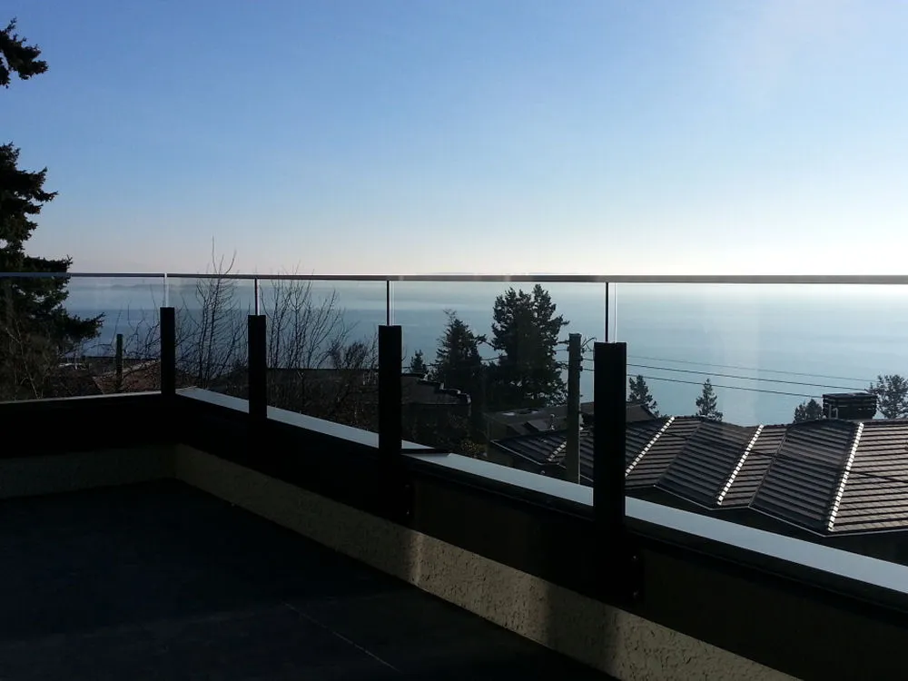 Rooftop with a glass railing and a breathtaking view of the sea, rooftops, and trees under a clear
