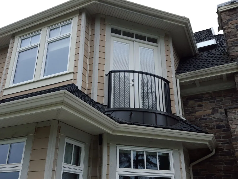 Second story French doors open onto a small Juliet balcony with a black metal railing, above a bay