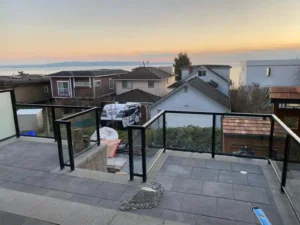 Residential patio with customizable aluminum railings overlooks neighboring houses and water in the background at sunset in Langley BC. Stones and construction materials are visible on the patio area.
