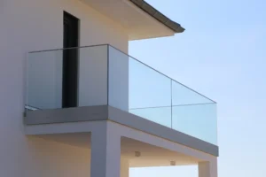 Modern house balcony with glass railings and white walls, viewed from an angle against a clear blue sky, designed with safety in mind for children.