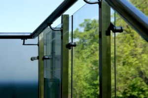 Close-up view of glass panels and metal supports on a structure with trees and blue sky visible in the background.